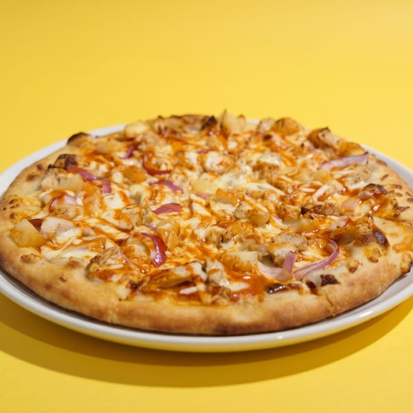 A BBQ chicken pizza with red onions and pineapple on a white plate against a yellow background.