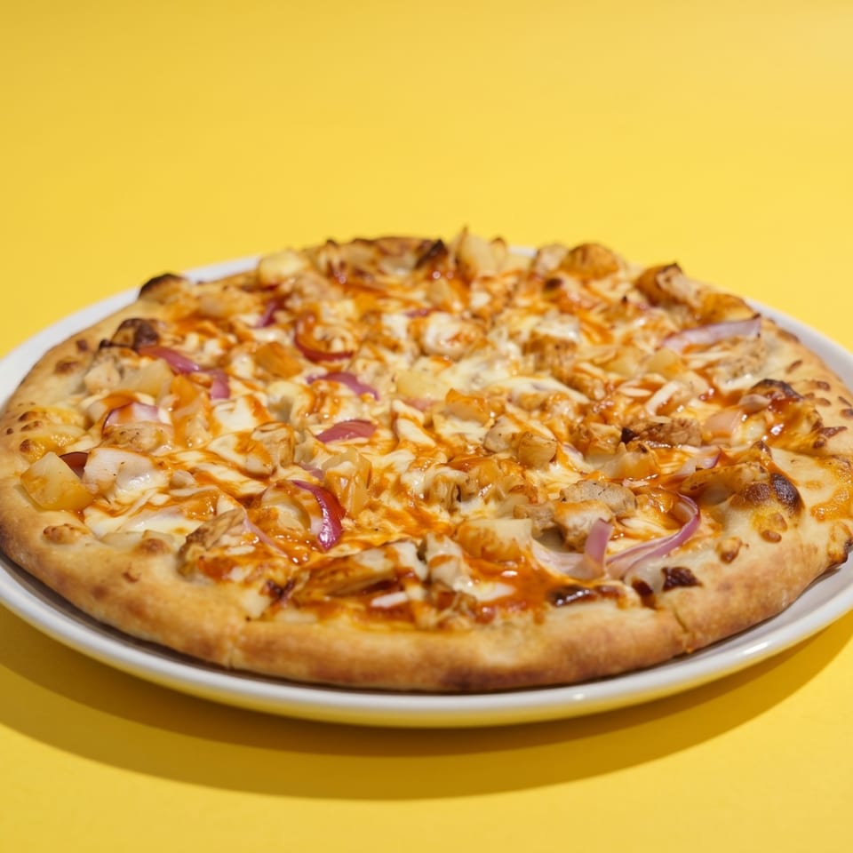 A BBQ chicken pizza with red onions and pineapple on a white plate against a yellow background.